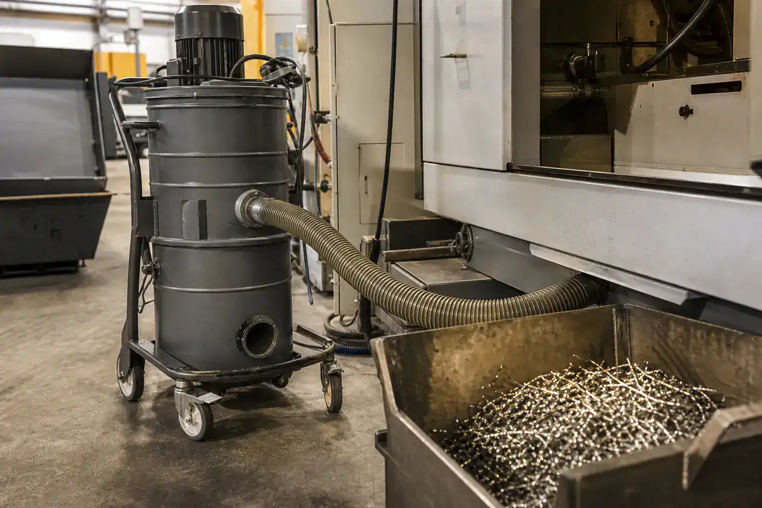 Groupe d'aspiration industrielle raccordé à une machine-outil, bac à copeaux métalliques ouvert au premier plan