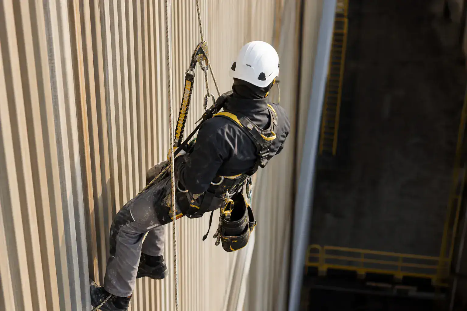 Cordiste en cours de descente le long d'un bardage d'usine, cordes et absorbeur bien visibles