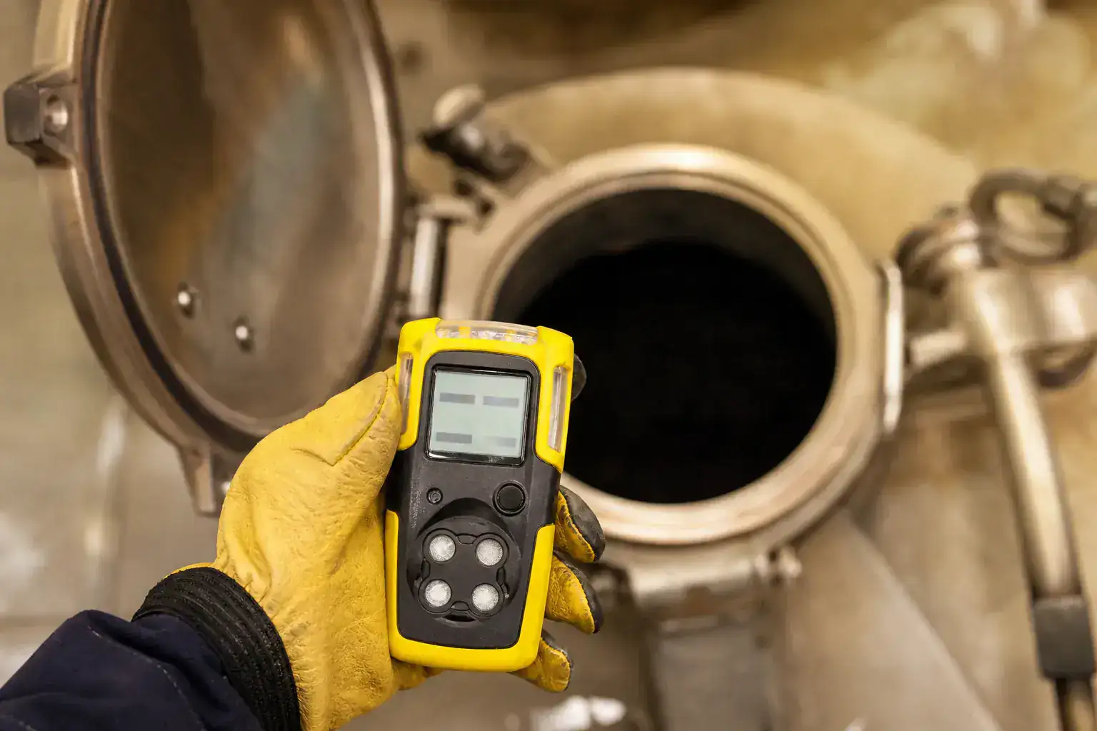 Détecteur de gaz portatif tenu devant une trappe d'accès, écran allumé, main gantée